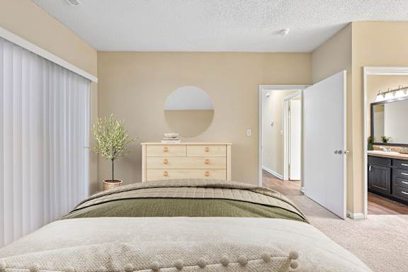 A bedroom with a bed, dresser, mirror, and a plant.