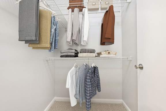 A white closet with clothes hanging on a rod.