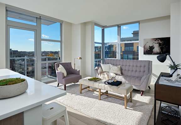 A modern living room with a grey sofa, a white table, and a large window with a view of the city.