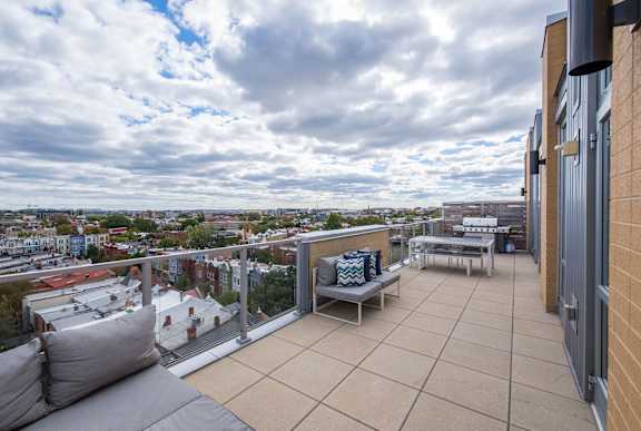 A balcony with a grey couch and a blue and white striped pillow overlooks a cityscape.