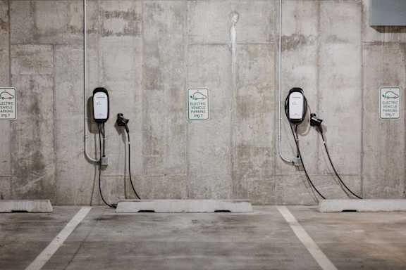 Three electric vehicle charging stations are lined up against a concrete wall.