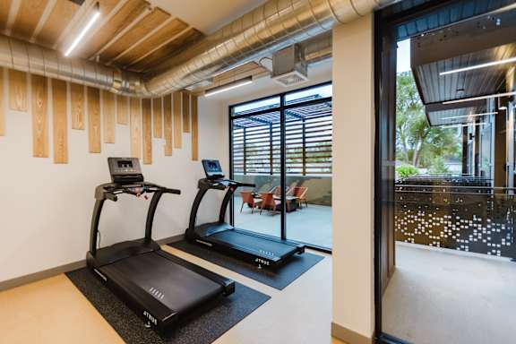Two treadmills in a room with wooden wall paneling and a view of the outdoors.