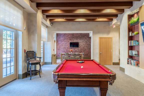 A pool table is in the middle of a room with a chair and a window