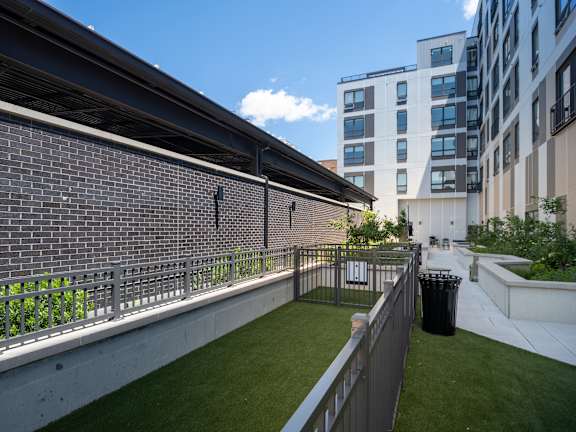 A small green space with a fence and a trash can is surrounded by buildings.