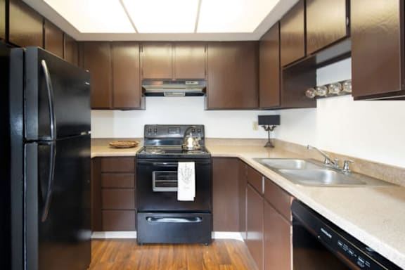 A black refrigerator is in a kitchen with brown cabinets.at Country Woods, Ogden, UT 84401