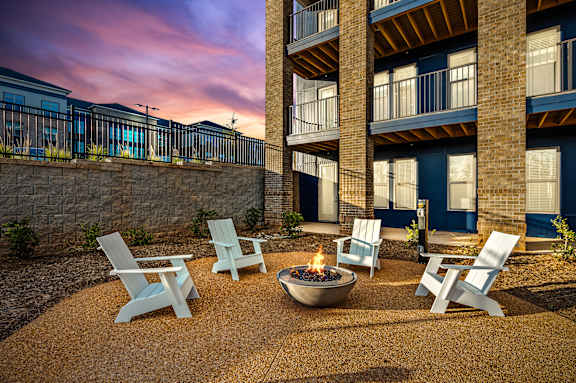 A fire pit sits in the middle of a gravel patio surrounded by four chairs.