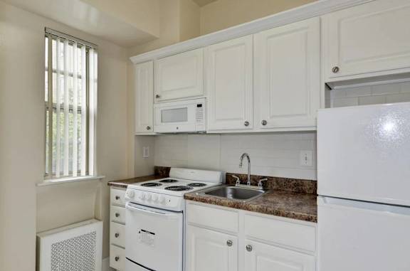 A white kitchen with a stove, sink, and cabinets.