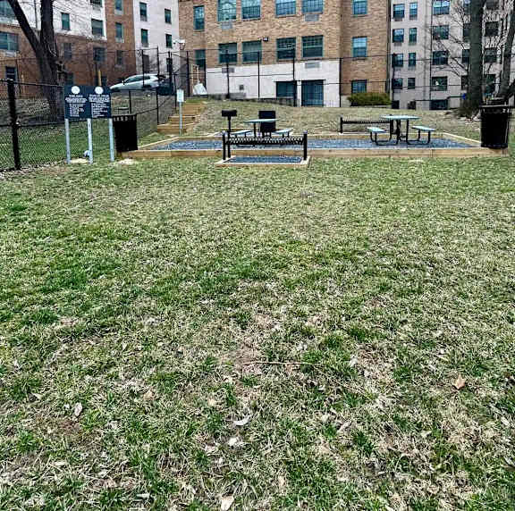 A grassy area with a picnic table and a fence in front of a building.