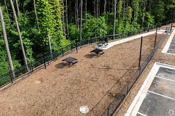 A black fence surrounds a dirt field with a picnic table and a trash can.