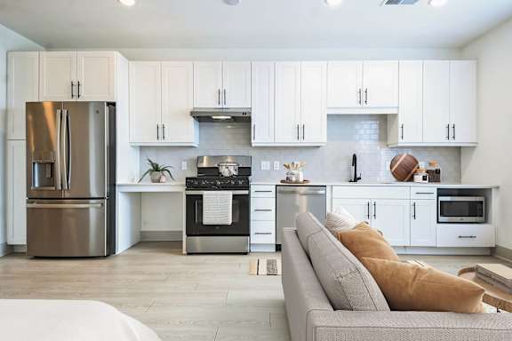 a white kitchen with stainless steel appliances and a couch at Metropolitan at the Riverwalk, Wilmington, NC