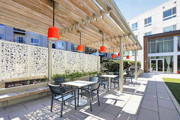 A patio with a table and chairs under a wooden canopy.