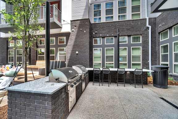A patio with a grill and chairs is surrounded by buildings.