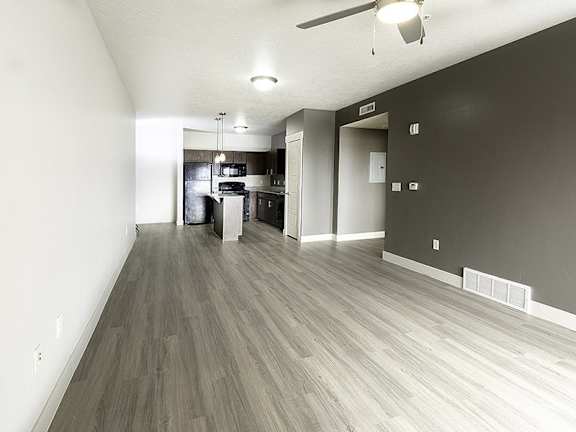 A room with a kitchen in the background and a long hallway with wood floors.