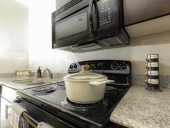 A pot is on a stove with a microwave and oven above it.