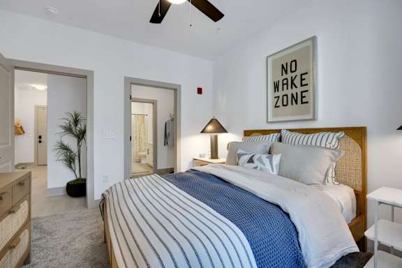 A bedroom with a bed, a ceiling fan, and a "NO WAKE ZONE" sign on the wall.