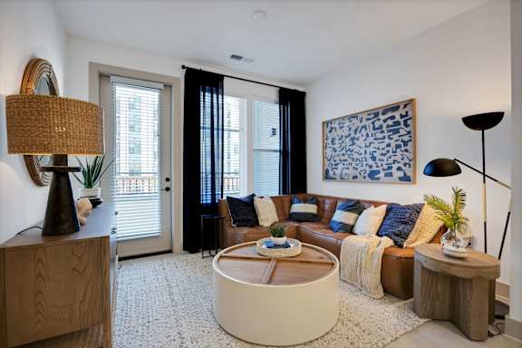 A living room with a brown sofa, a round coffee table, and a blue and white patterned painting on the wall.