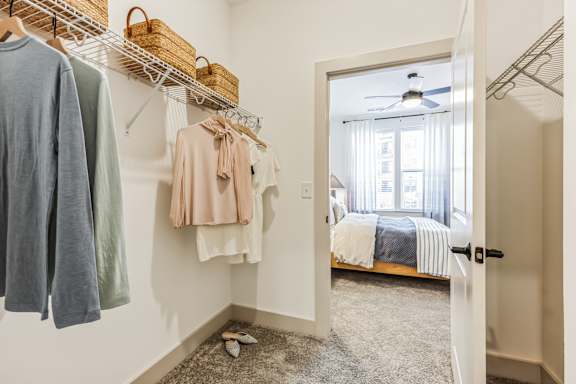 A bedroom with a bed, a window, and a closet with clothes hanging.