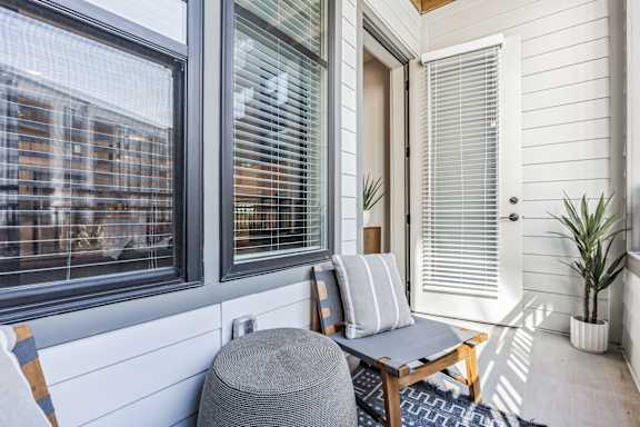 A patio with a chair and a table with a cushion and a potted plant.
