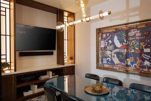 A room with a television, a painting, and a table with chairs.