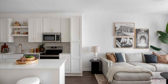 A modern kitchen with white cabinets and a grey sofa in the living room.