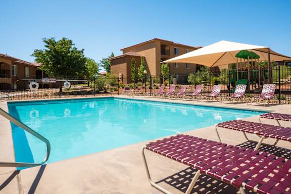 A pool with a white umbrella and red chairs at West Park Apartments, New Mexico