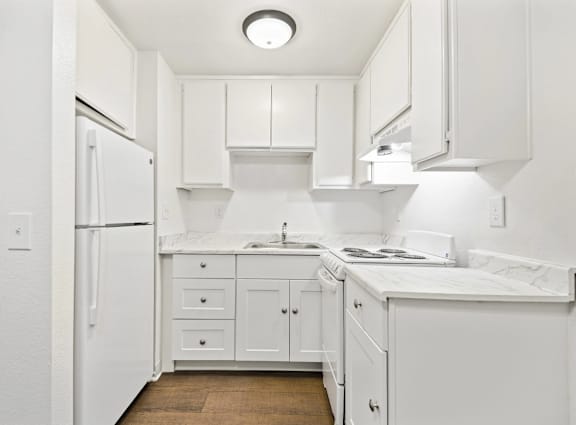 A white kitchen with a refrigerator, sink, and cabinets.