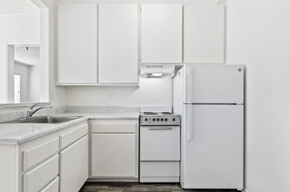 A white kitchen with a refrigerator, sink, and stove.