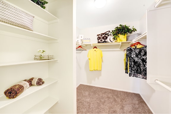 a walk in closet with white shelves and a yellow shirt on a rack