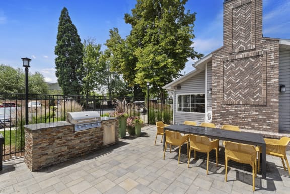 a patio with a grill and a table with yellow chairs