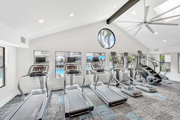 A spacious gym with treadmills, elliptical machines, and a fan.