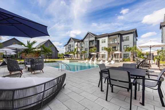 A poolside area with chairs and a table is surrounded by modern buildings.