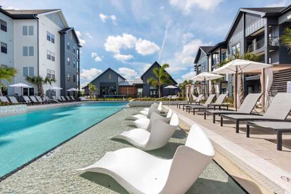 A row of white chairs are lined up by a pool.