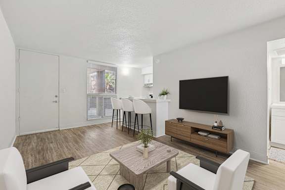 A living room with a white couch, a wooden coffee table, and a flat screen TV mounted on the wall.