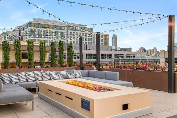A modern outdoor seating area with a fire pit and string lights.