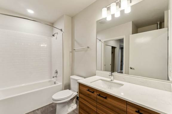 A white bathroom with a toilet, sink, and mirror. at Ion Town Center, Shoreline, WA