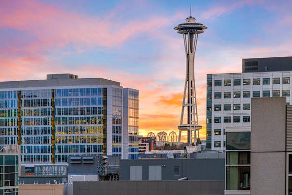 The Space Needle stands tall in front of a building with a sunset sky in the background.