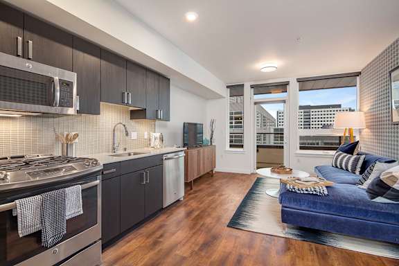 A modern kitchen with dark wood cabinets and a blue sofa in the living room.