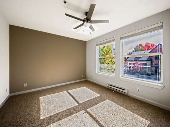 A room with a ceiling fan and two windows.