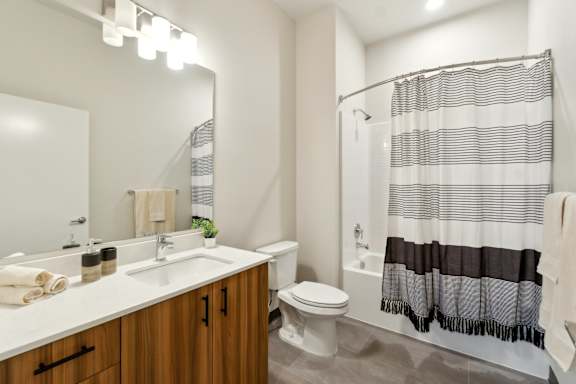 A bathroom with a white sink, a white toilet, and a shower with a black and white striped shower curtain. at Ion Town Center, WA
