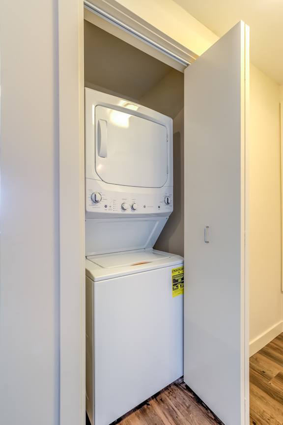 A white dishwasher is in a narrow space between a wall and a cabinet.
