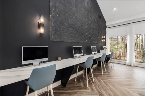 a long desk with computers and chairs in a room with a window