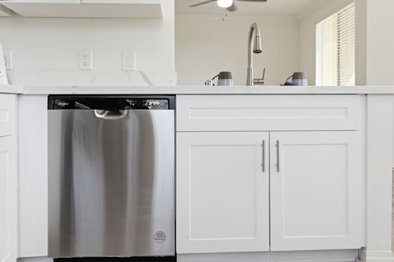 A stainless steel dishwasher is in a kitchen with white cabinets.
