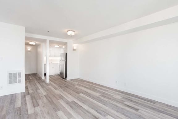 an empty living room with a refrigerator in the corner