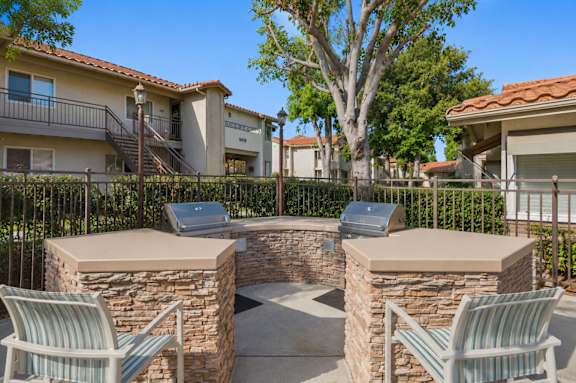 An outdoor grilling area with two grills and chairs.