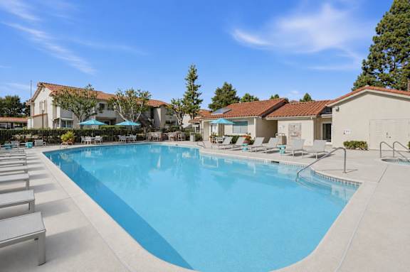 A resort style swimming pool with lounge chairs and umbrellas.