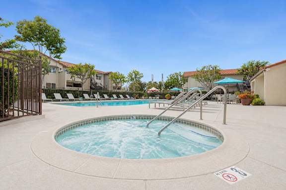 A relaxing spa next to a pool with lounge chairs and umbrellas.