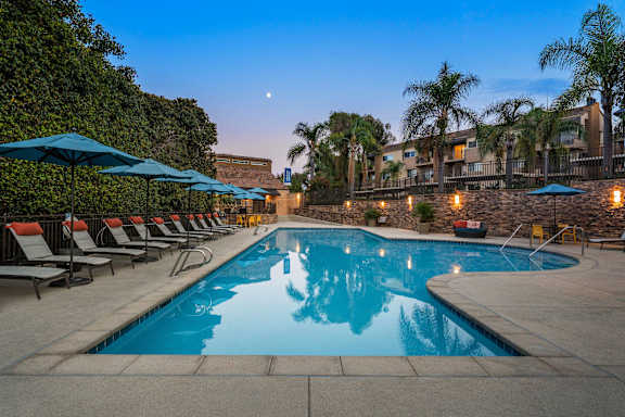 A swimming pool surrounded by lounge chairs and umbrellas at dusk.