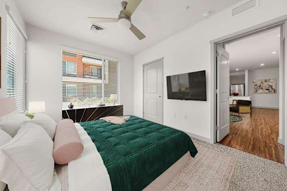 A bedroom with a bed, a ceiling fan, and a window with blinds.