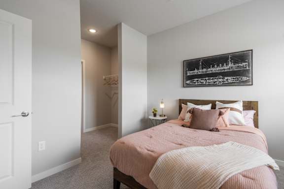 A bedroom with a pink bedspread and a framed picture on the wall.