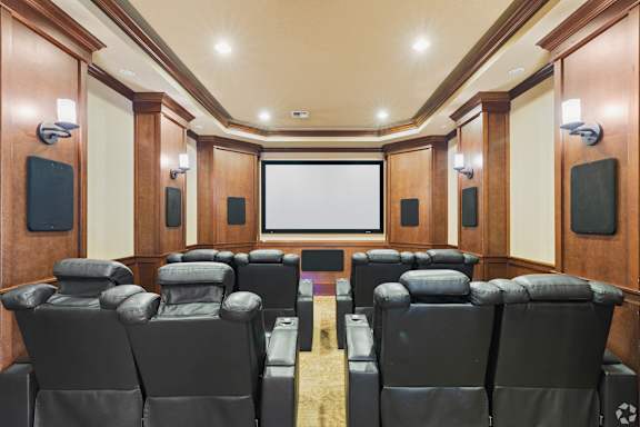 A row of black cinema seats are arranged in front of a large screen.